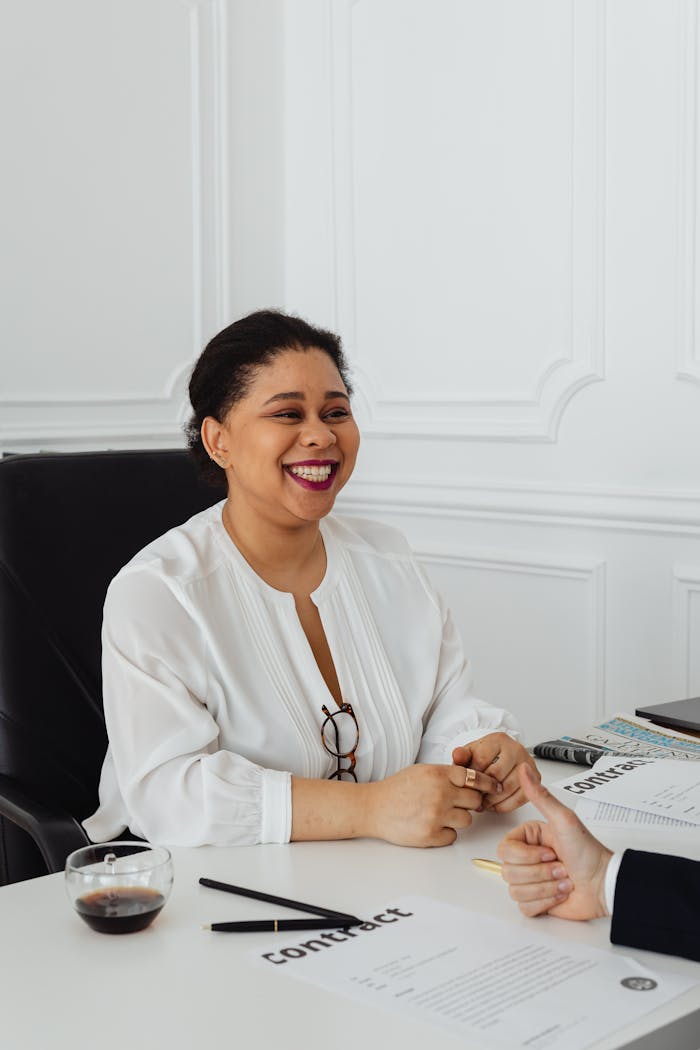 Confident businesswoman in white blouse smiling while signing contract in office setting.